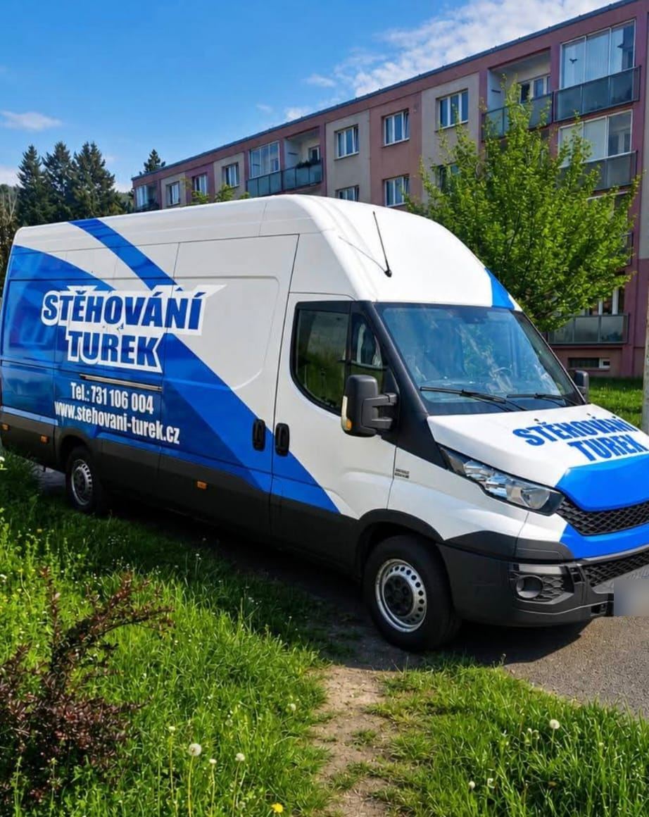 Bílá dodávka Stěhování Turek s modrým polepem před panelovým domem