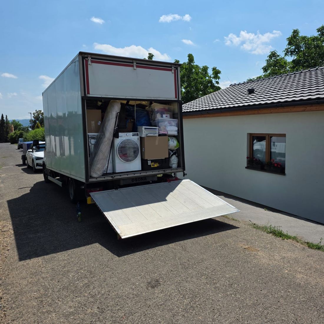 Skříňový vůz s hydraulickým čelem naložený nábytkem a krabicemi u rodinného domu