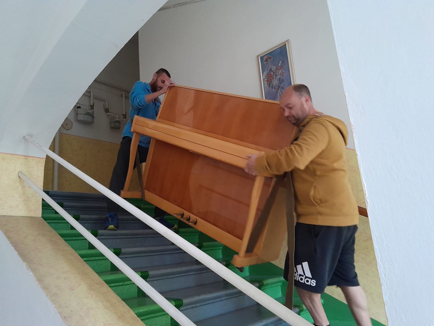 Dva stěhováci nesou pianino po schodech na popruzích