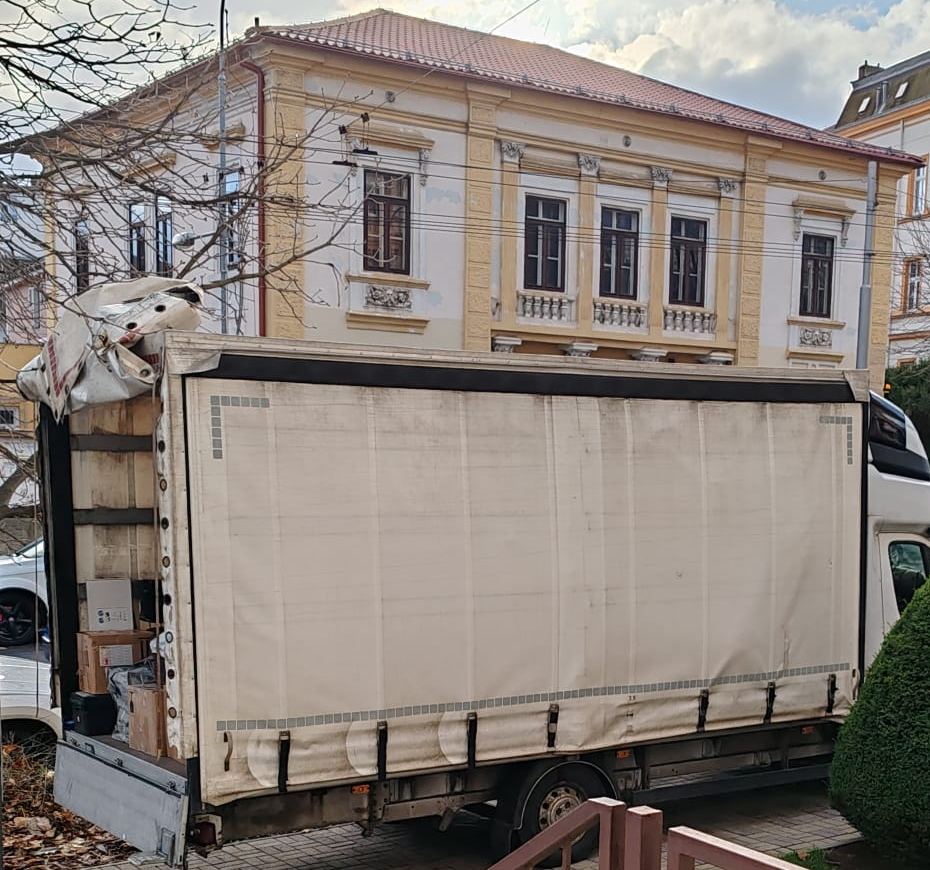 Plachtový vůz s krabicemi a nábytkem zaparkovaný před městskou vilou