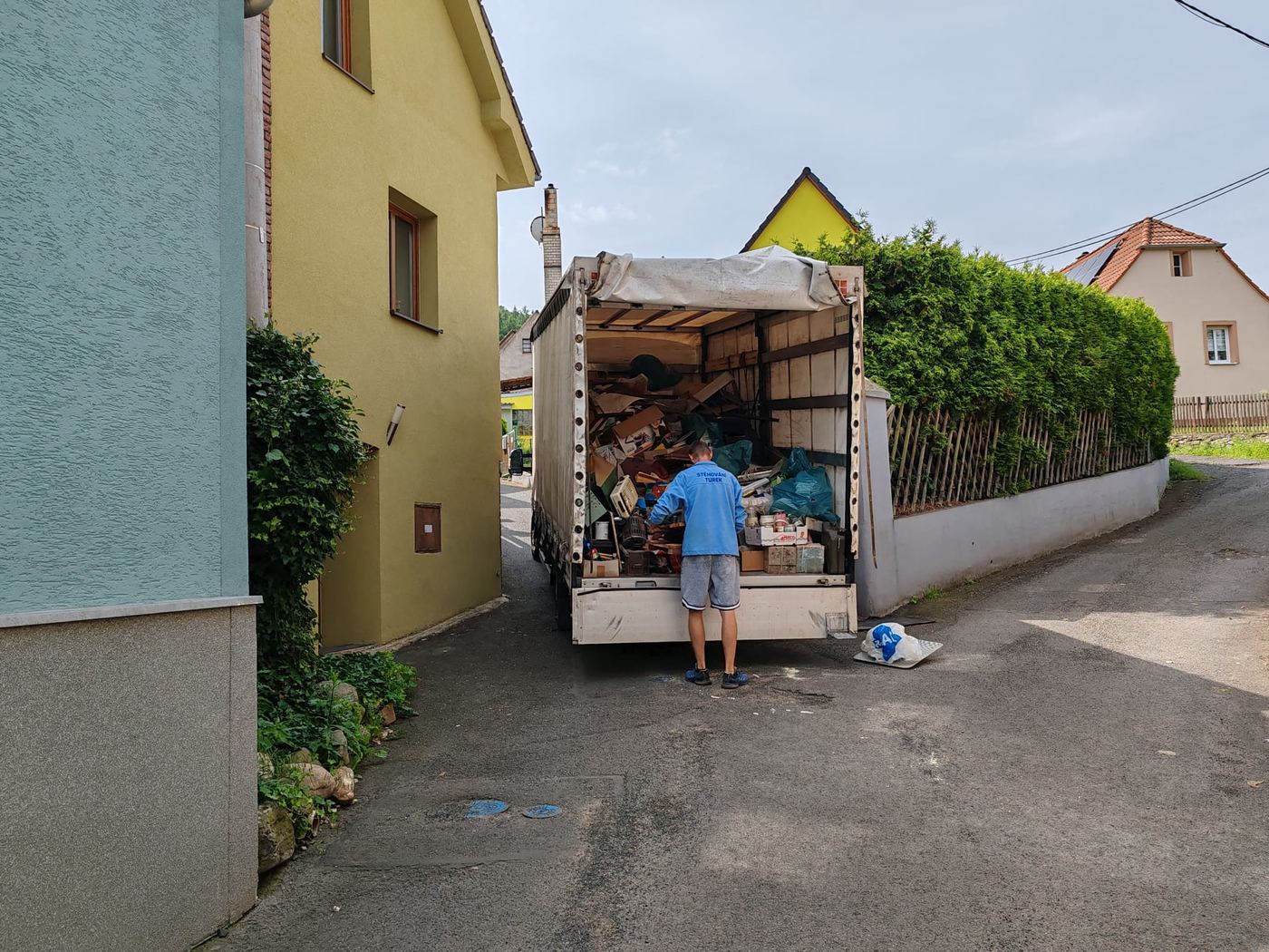 Stěhovák v modré mikině Stěhování Turek nakládá vyklizené věci do vozu